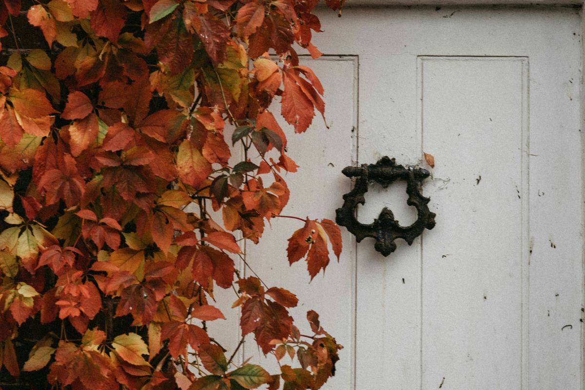 A white painted door with a vintage iron knocker, framed by rich autumn foliage in deep reds and golds