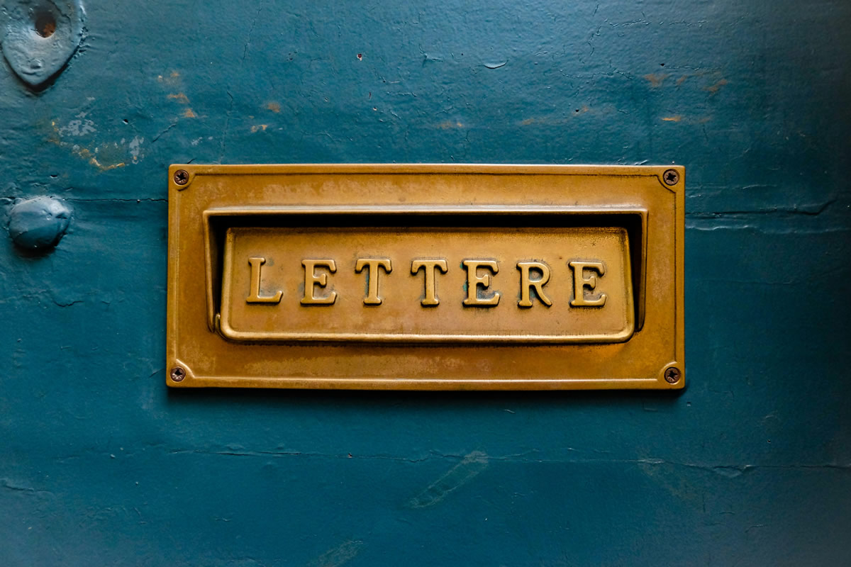 A vintage brass letter slot reading 'Lettere' set into a weathered teal door, warm and inviting