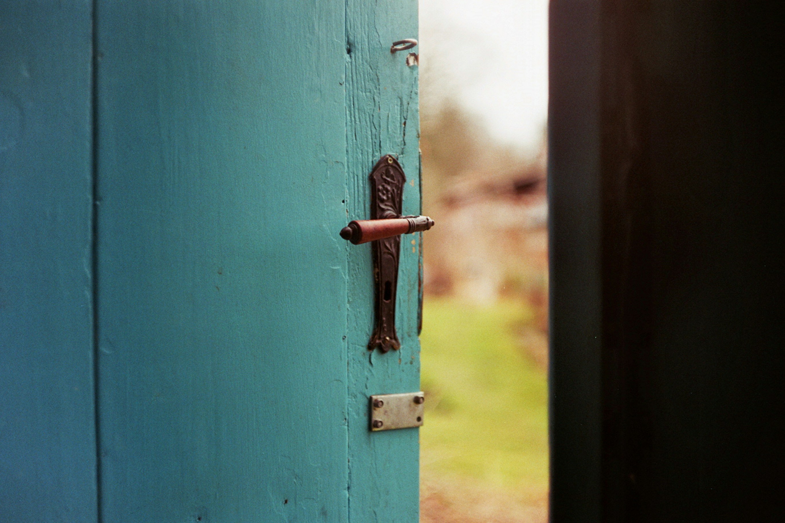 Teal door with vintage handle, slightly ajar
